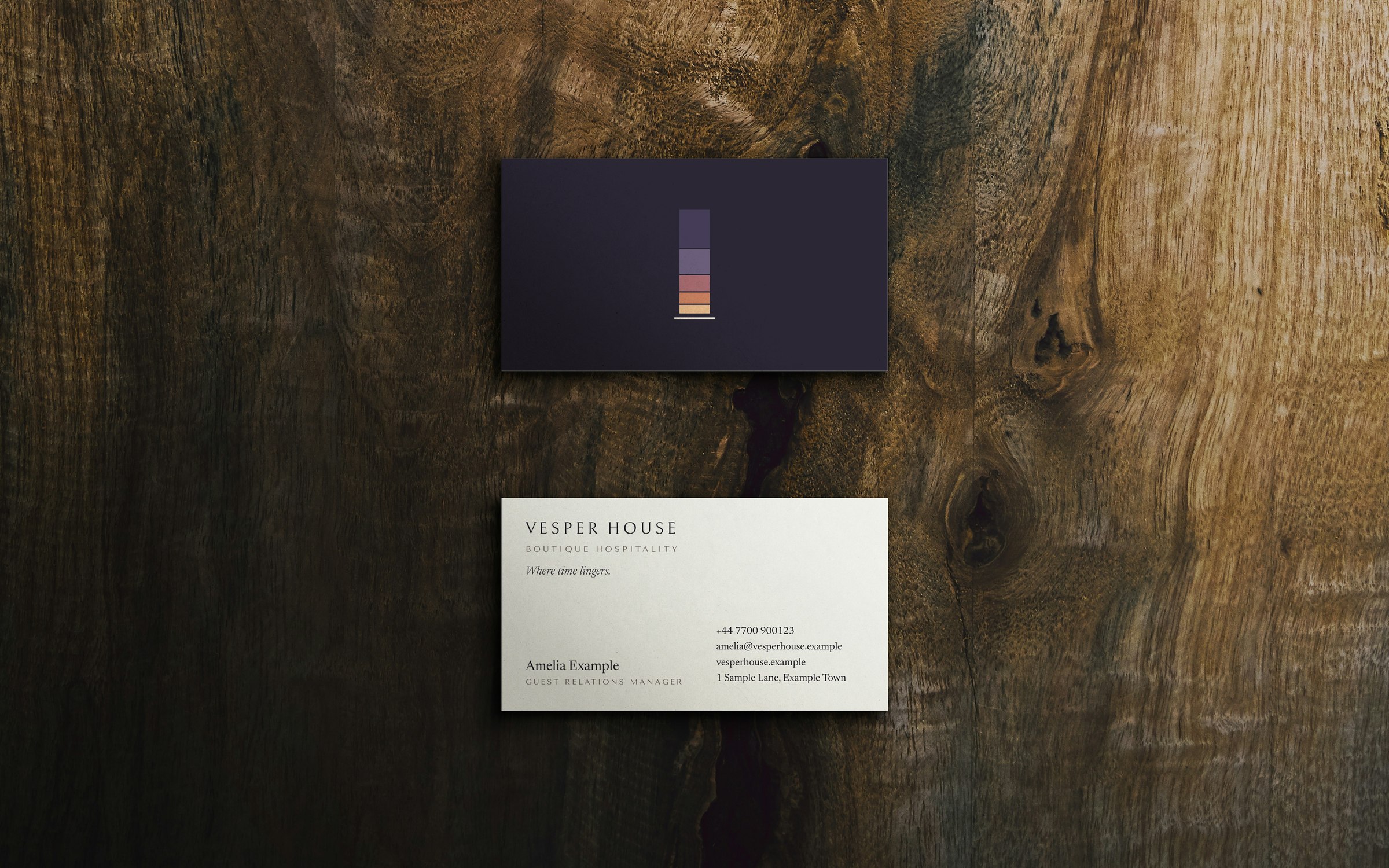 Two Vesper House business cards on walnut: a night-blue front with the window symbol and a white contact side reading Vesper House, Boutique Hospitality, Where time lingers.