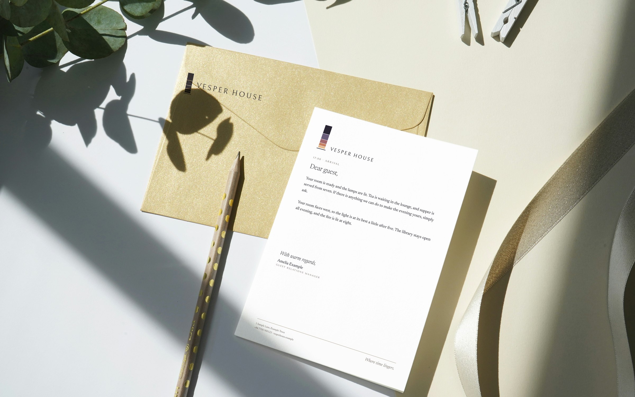 A Vesper House letter to a guest on white paper, beside an envelope printed with the logo, in soft morning light.